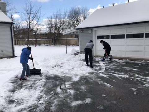 A group of refugee youth help to shovel snow from community driveways.